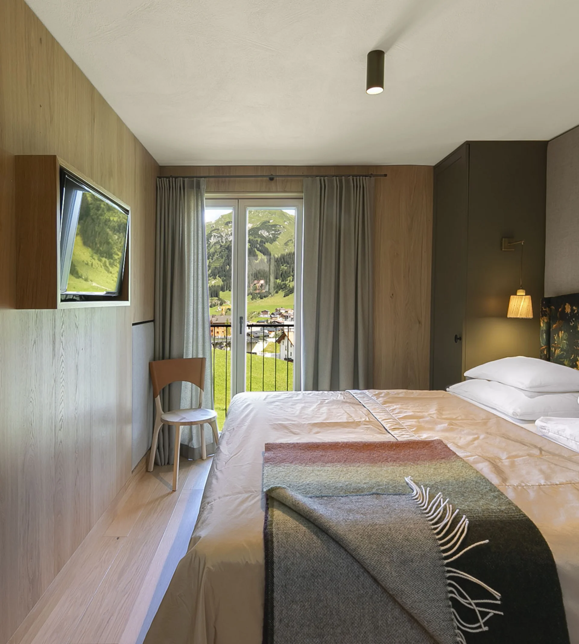 Ihr Hotel in Lech am Arlberg. Das Sunora. Modernes Hotelzimmer mit Doppelbett, Holzverkleidung und Balkon mit Blick auf Berge