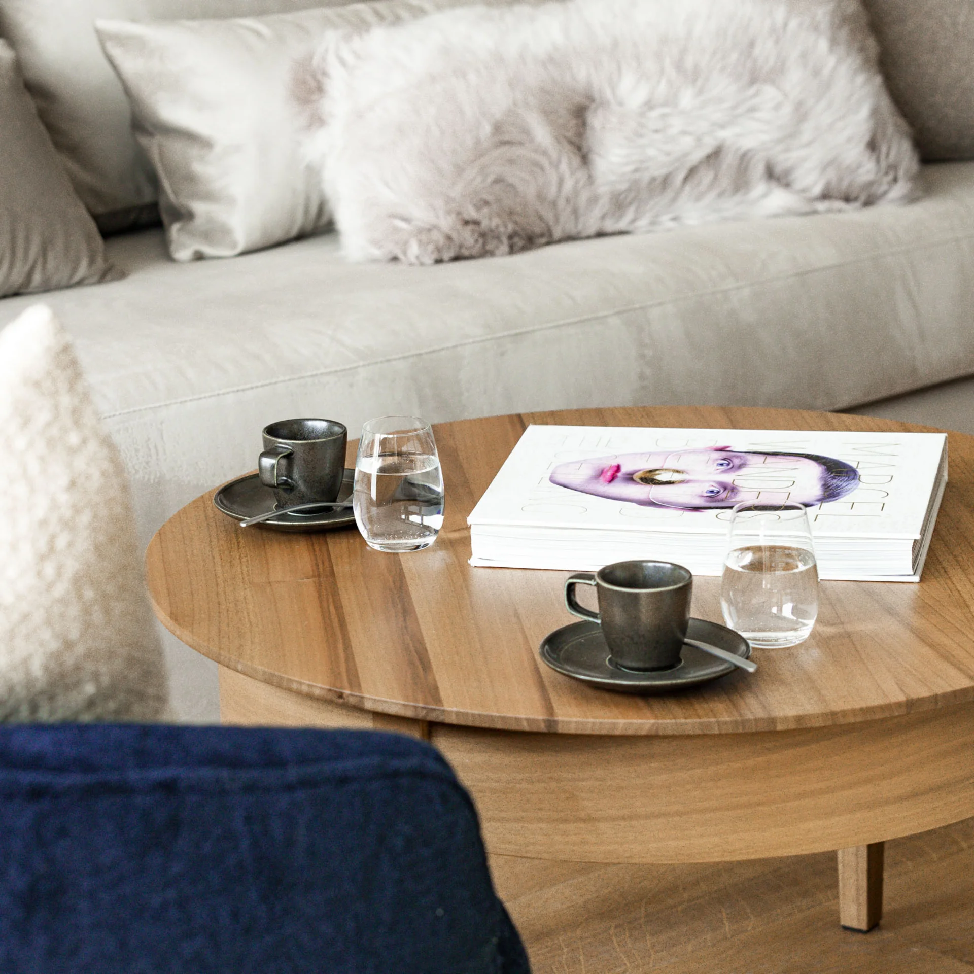 Ihr Hotel in Lech am Arlberg. Das Sunora. Wohnzimmer mit beigem Sofa, flauschigen Kissen und Holz-Couchtisch mit Tassen