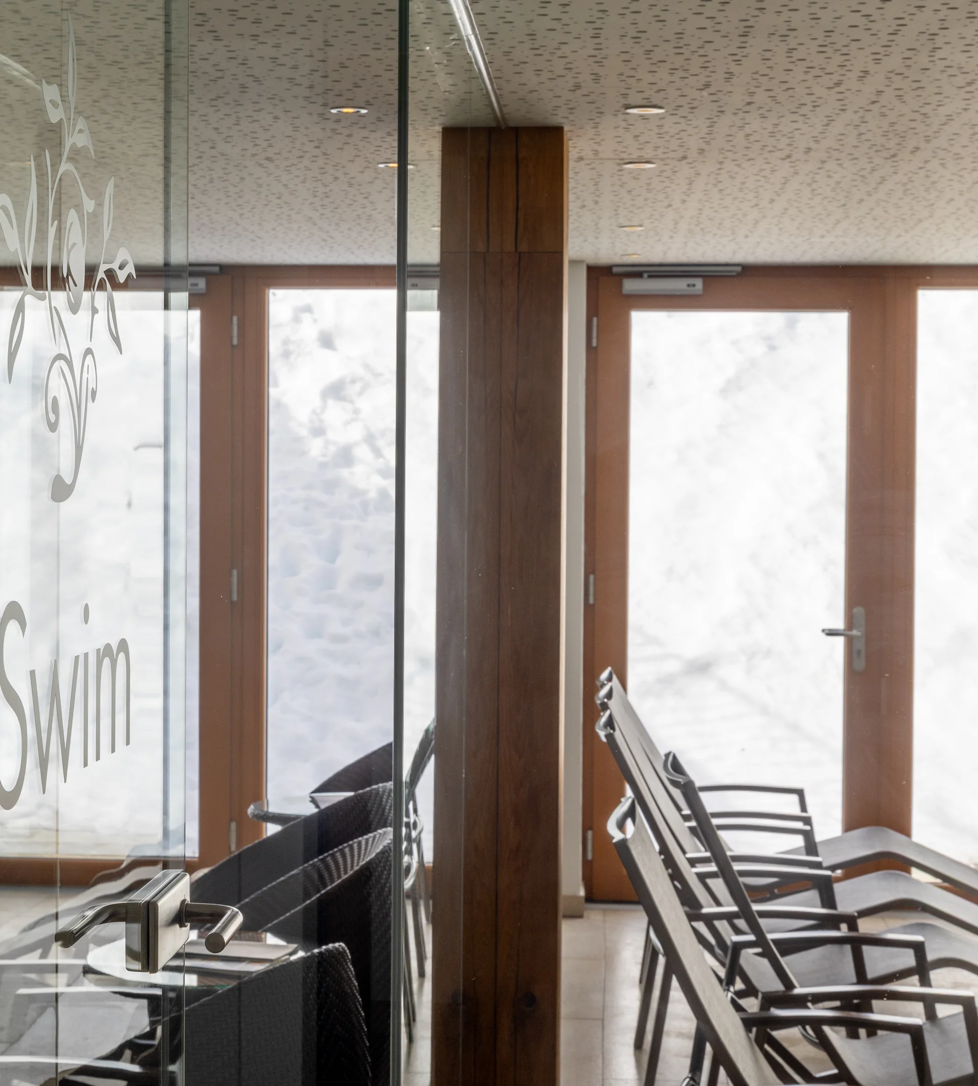 Ihr Hotel in Lech am Arlberg. Das Sunora. Ruhebereich mit Liegestühlen und Glasscheibe im Schwimmbad