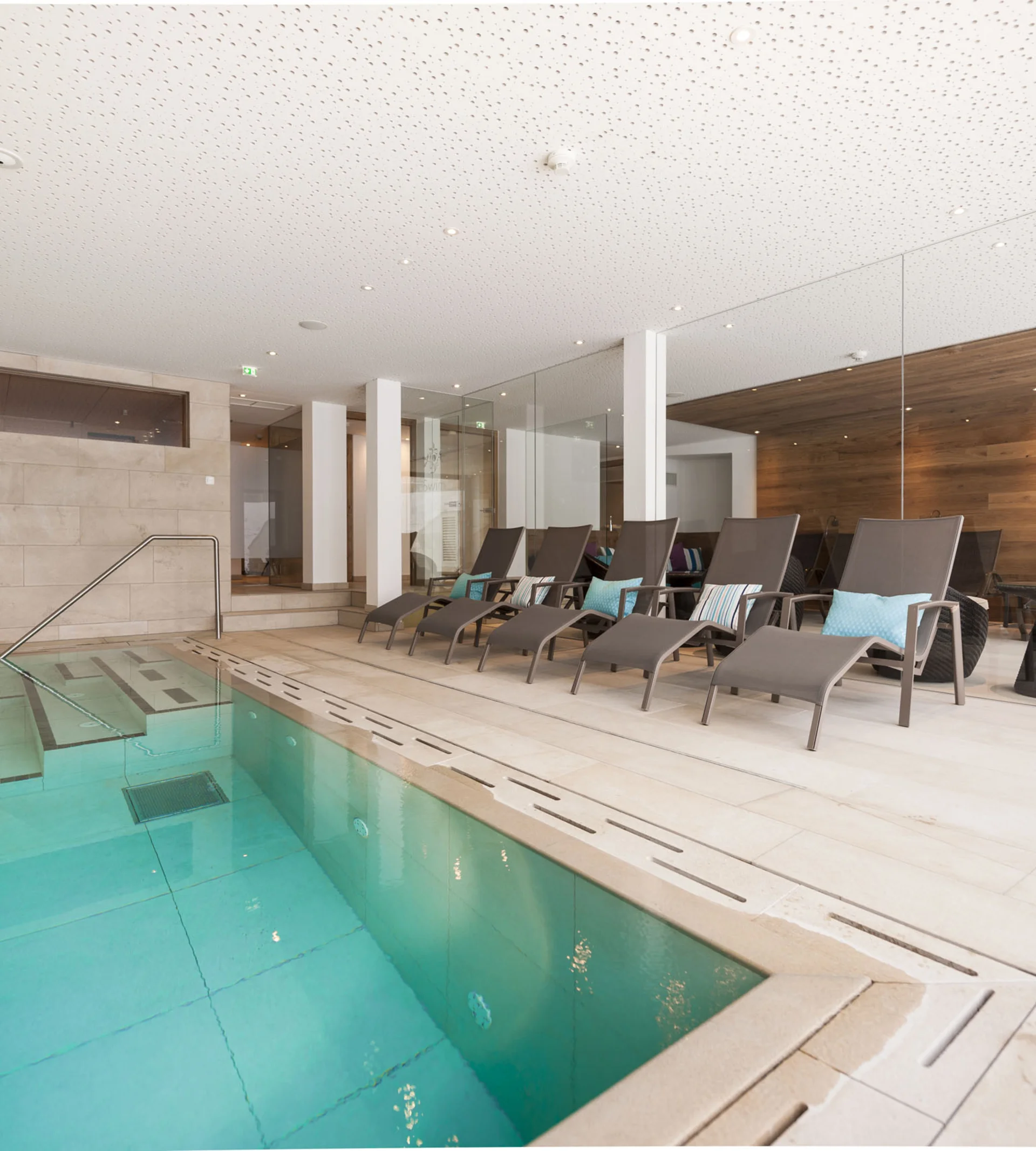 Ihr Hotel in Lech am Arlberg. Das Sunora. Moderner Innenpool mit Liegestühlen und Holzverkleidung an der Wand