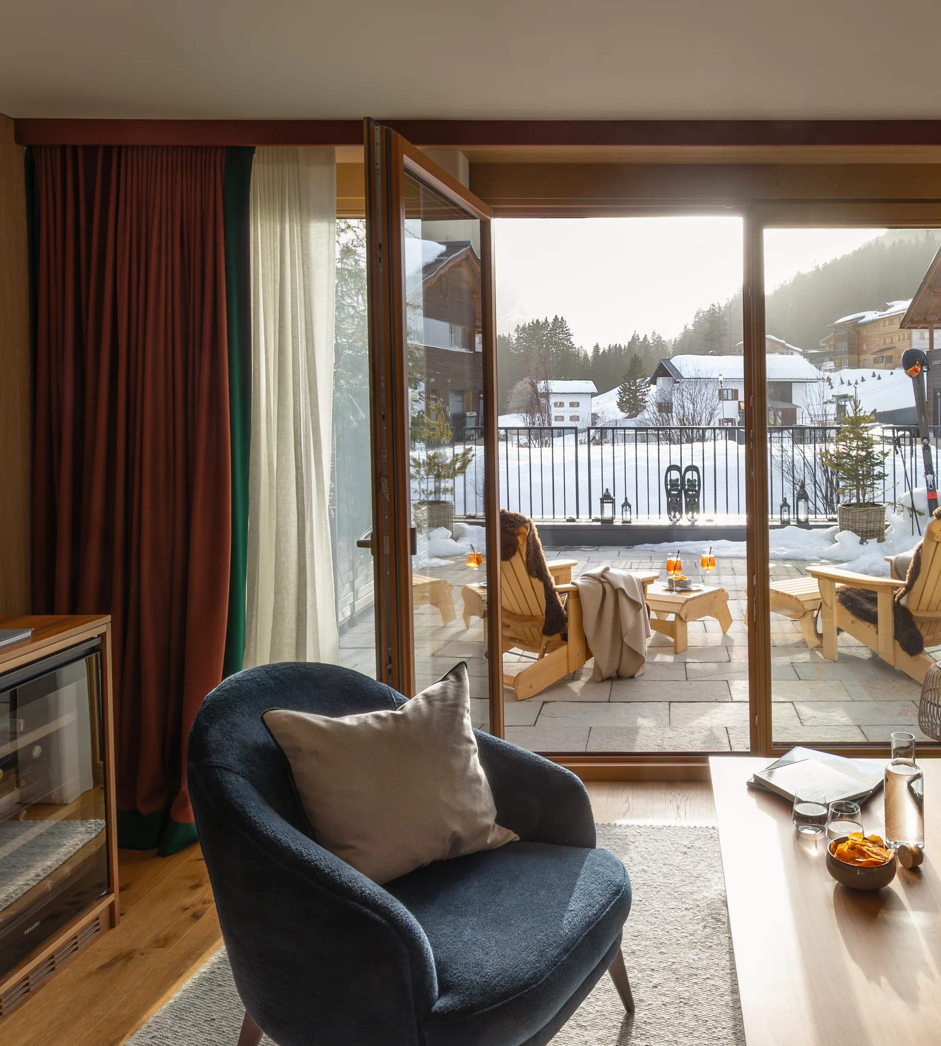 Ihr Hotel in Lech am Arlberg. Das Sunora. Gemütlicher Wohnbereich mit offenem Balkon und Blick auf verschneite Häuser und Berge