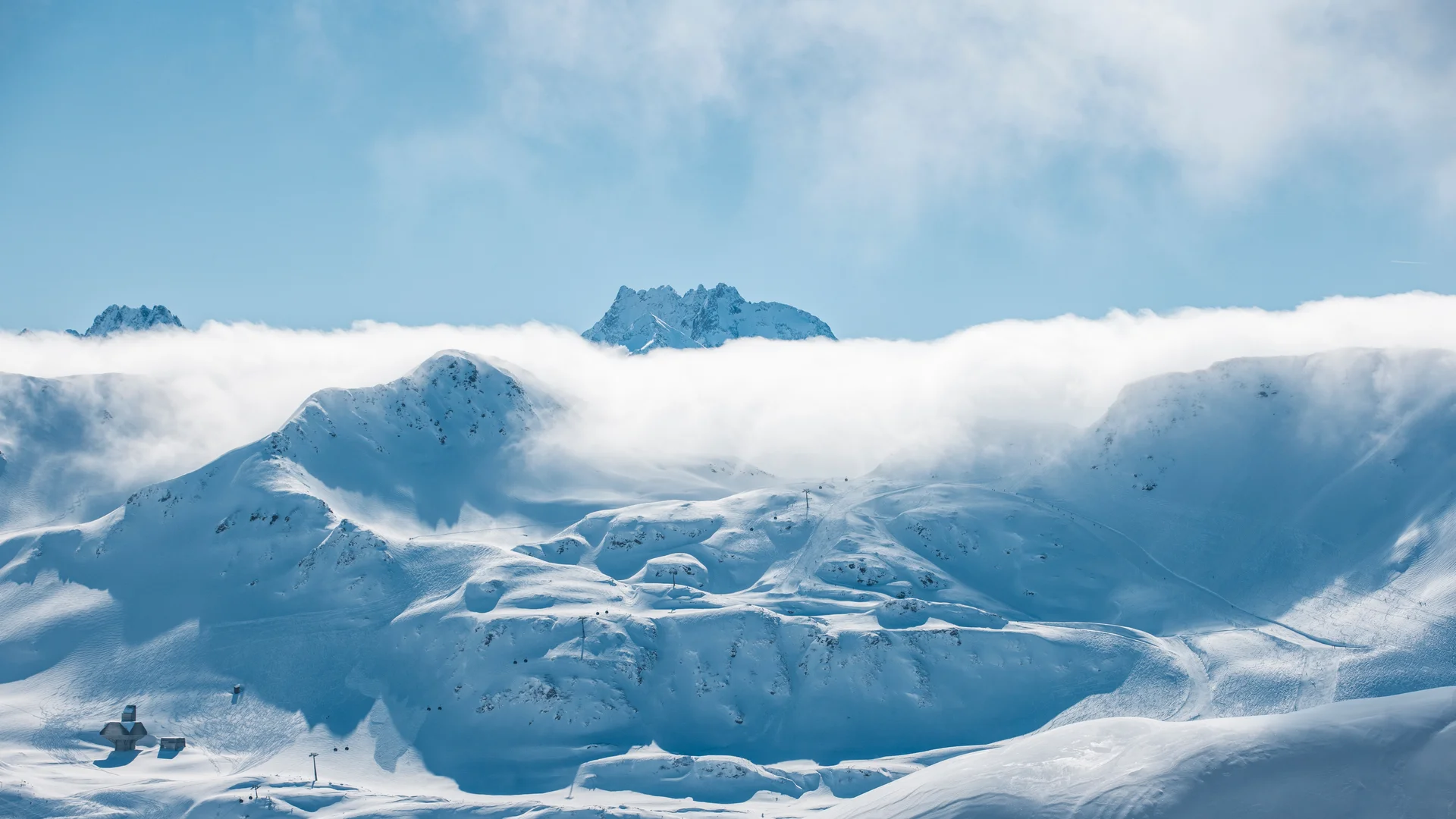Ihr Hotel in Lech am Arlberg. Das Sunora. Schneebedeckte Berge mit Wolken und blauem Himmel im Hintergrund