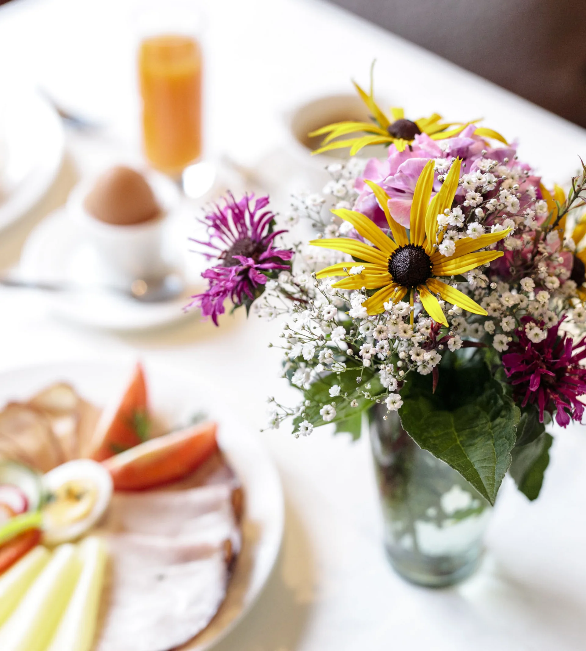 Ihr Hotel in Lech am Arlberg. Das Sunora. Bunter Blumenstrauß in Glasvase auf gedecktem Frühstückstisch