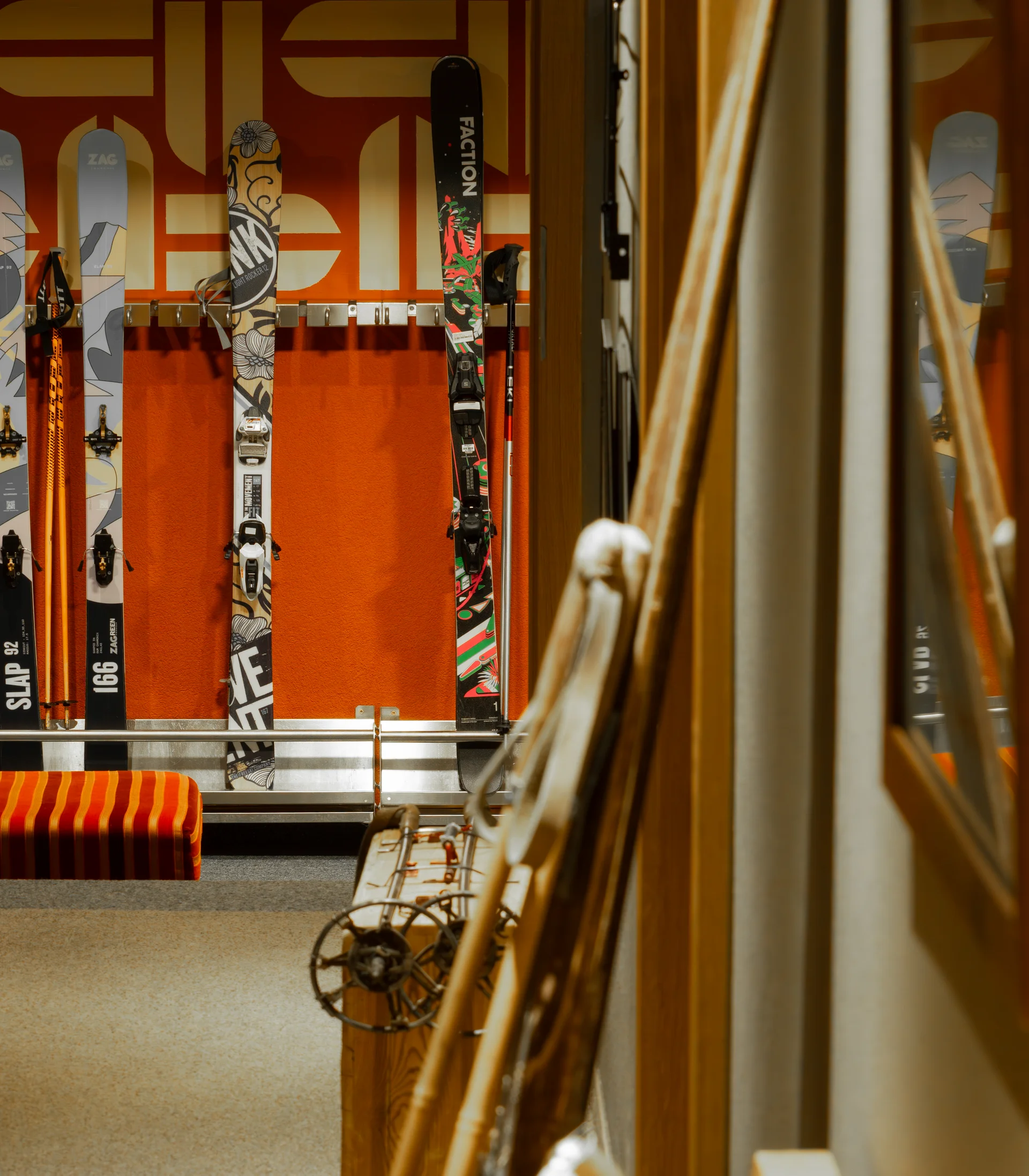 Ihr Hotel in Lech am Arlberg. Das Sunora. Skier und Skistöcke in einem Skiraum mit orangefarbenem Hintergrund