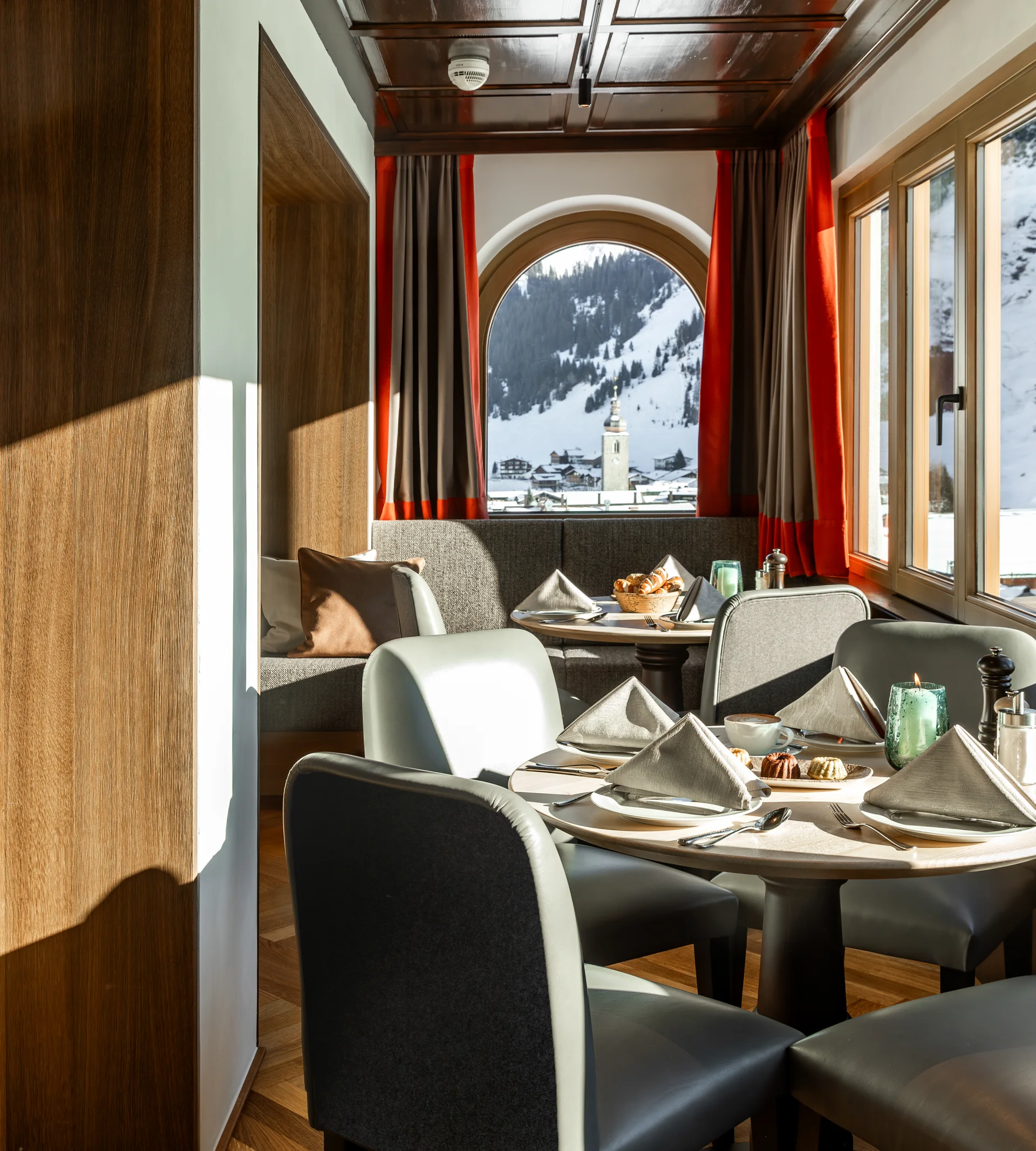 Ihr Hotel in Lech am Arlberg. Das Sunora. Gemütlicher Essbereich mit Bergblick durch große Fenster in einem Holzdekor-Restaurant